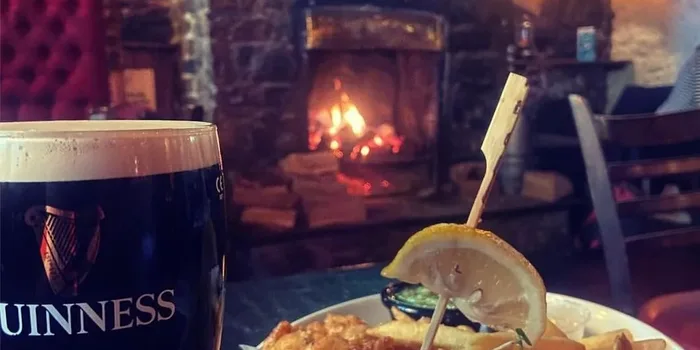 a pint of guinness and fish and chips in a pub, with an open fire in the background