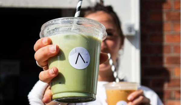 person holding a plastic cup with iced matcha and a straw