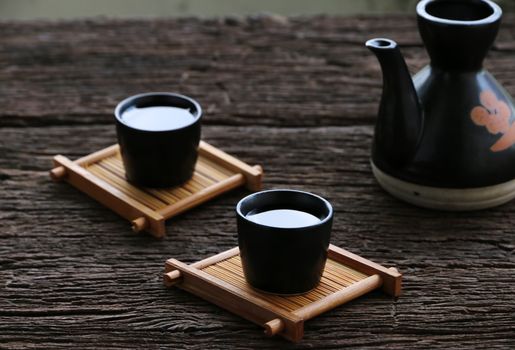 black teapot and two black cups with sake, placed on small wooden coasters