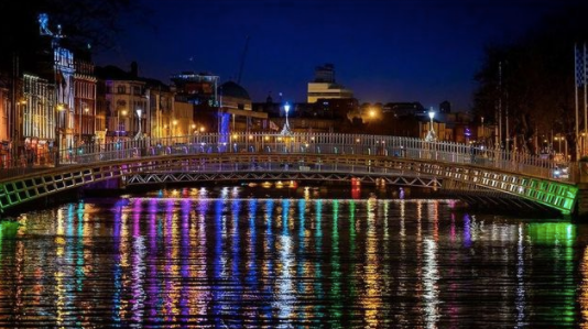 the ha'penny bridge in dublin at night, multicoloured lights reflected in the water of the liffey