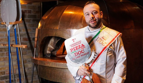 man holding award in front of a pizza oven