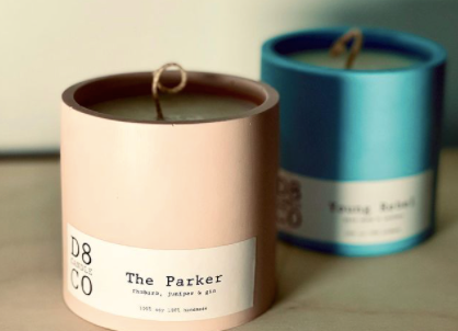 two candles in ceramic pots placed one in front of the other, one pale pink and one blue. The label of the candle in front reads "The Parker"