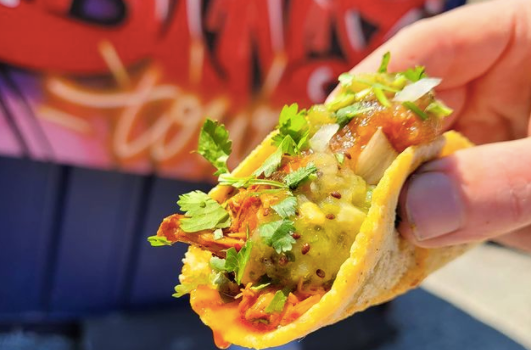 close up of a taco loaded with cheese, meat and coriander. Street art in background
