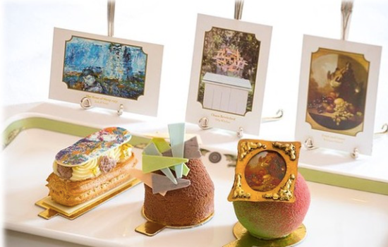 eclairs and buns topped with miniature works of art - one is a watercolour, one an abstract collage and one a traditional painting in a mini ornate gold frame
