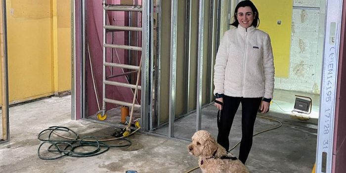 Woman and a dog standing in a restaurant in the process of being refurbished - exposed floors, ladders in the background, building equipment etc