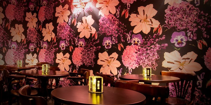 Interior of a bar with pink and brown floral wallpaper and tables and chairs with candleholders made from cassette tapes