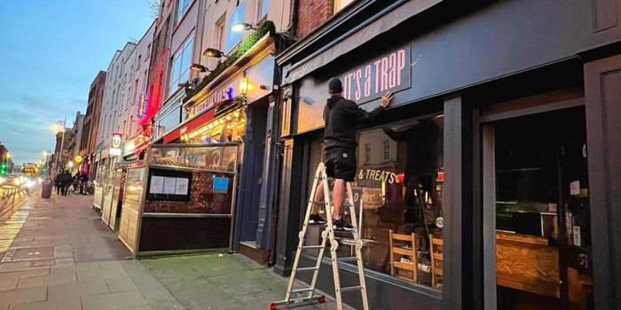 man on ladder adjusting a sign which reads "its a trap" on a black shop front