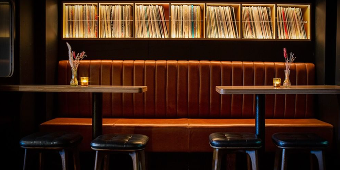 tan leather bar couch with high tables and stools in front of it, shelves stacked with vinyl records in the background