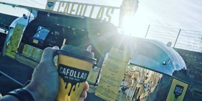 coffee cup held up outside cafollas food truck with sun shining in the background