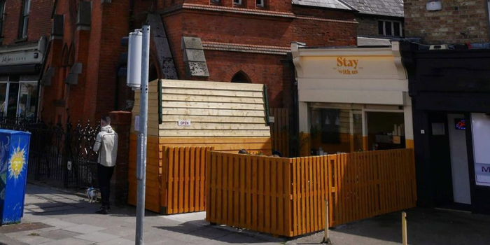 white cafe with "stay with us" painted above the door, and yellow wooden fencing surrounding it