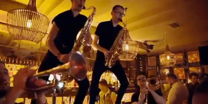 two trumpeteers playing on top of a bar in a busy nightclub