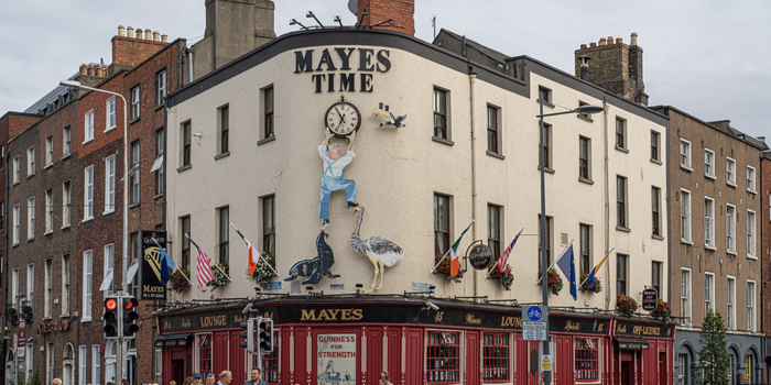exterior of Mayes Pub in Dublin - a red pub with white building above, a sign reads "Mayes Time" with a large clock below
