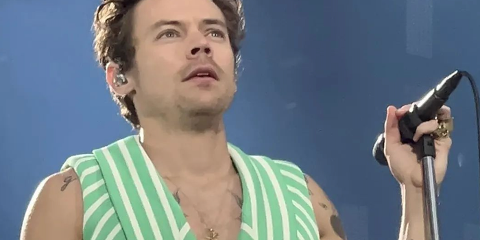 harry styles in green and white pinstriped sleeveless suit, holding a microphone and mic stand