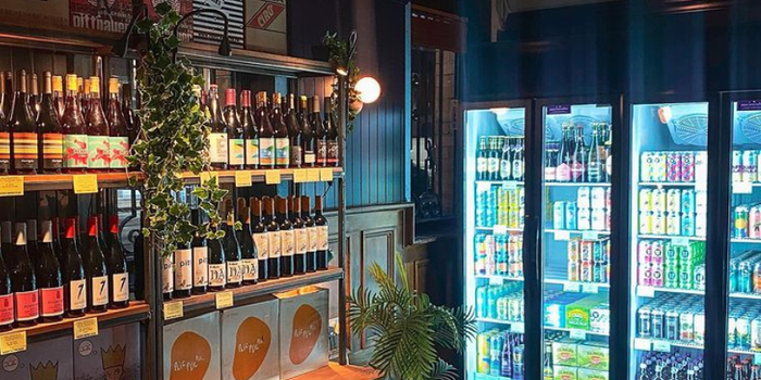interior of an off licence with shelves filled with wine bottles and a fridge full of colourful cans