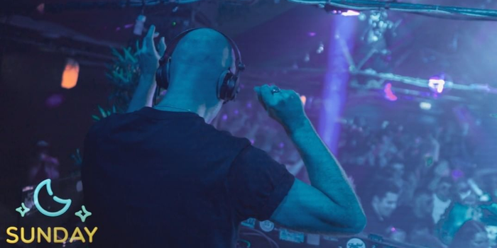 person dj'ing at a busy club night, crowd can be seen dancing in the background