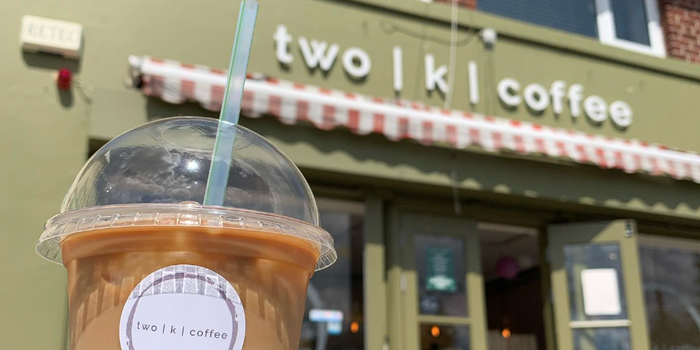 iced coffee cup with shop front of a cafe in the background, sign reads "two | k | coffee"