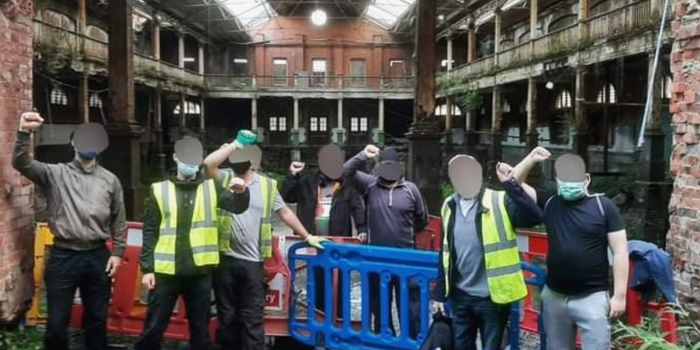 group of people with faces blurred out, some in hi vis vests, standing in front of the iveagh markets