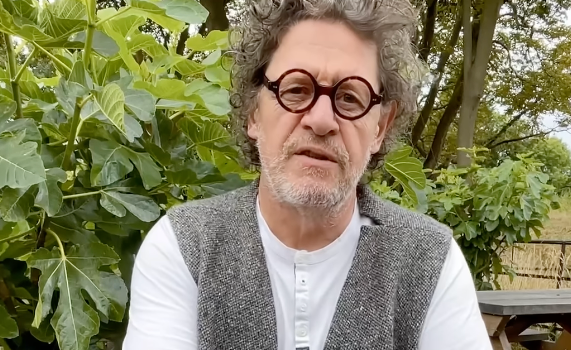 marco pierre white wearing a grey waistcoat and glasses, looking at camera