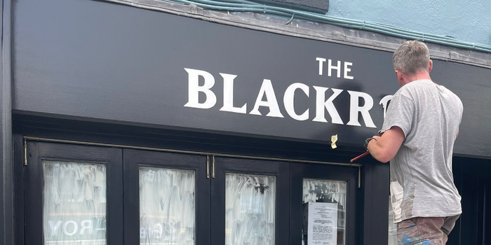 person painting signage which reads "The Blackrock" onto a black shop front