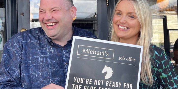 man and woman laughing and holding poster which reads "you're not ready for the glue factory yet, old horse" with Michaels logo above this