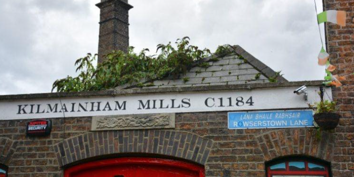 old brick building with red door and industrial style tower in background, with a sign that reads Kilmainham Mills C1184