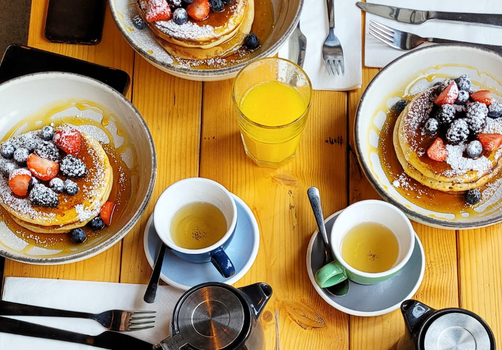 pancakes, juice and cups of tea on a brunch table