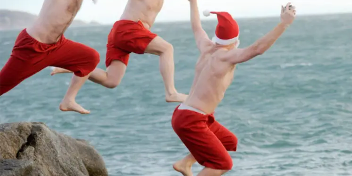 three men wearing santa hats and beards jumping off a rock into the sea