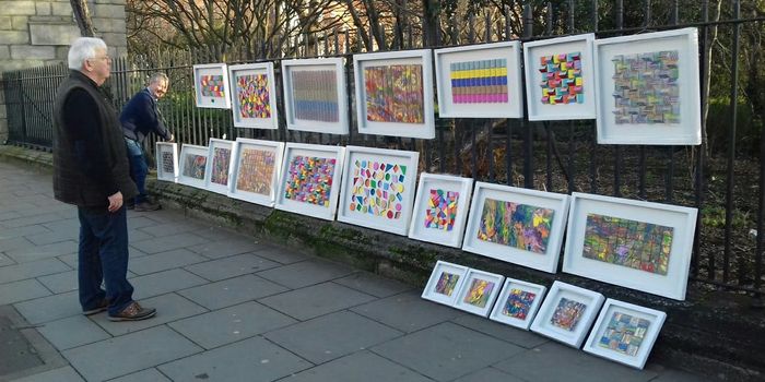 a series of framed artworks hanging on the railings outside a park at merrion square