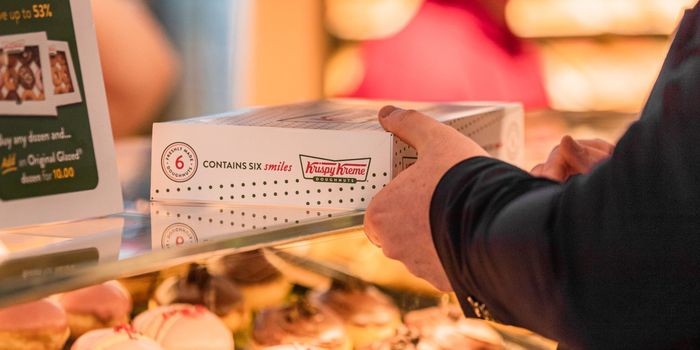 a person being handed a box of krispy kreme donuts over the glass counter, under which more donuts can be seen