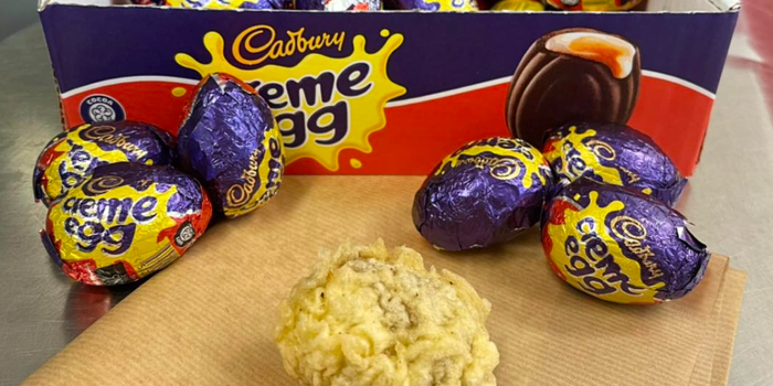 a box full of creme eggs with a battered one on a sheet of parchment paper in front of them
